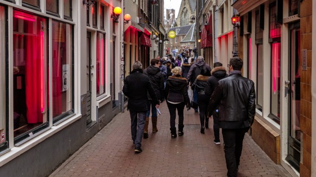 Turistas paseando por el barrio rojo de Ámsterdam, donde las prostitutas intentan atraer a los clientes desde detrás de su ventana.